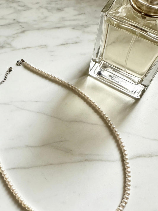 Minimalist 3-4mm round freshwater pearl necklace with 925 sterling silver clasp on marble next to perfume.